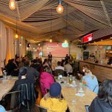 Saal von hinten mit einigen Zuschauern sichtbar - Huber auf der Bühne